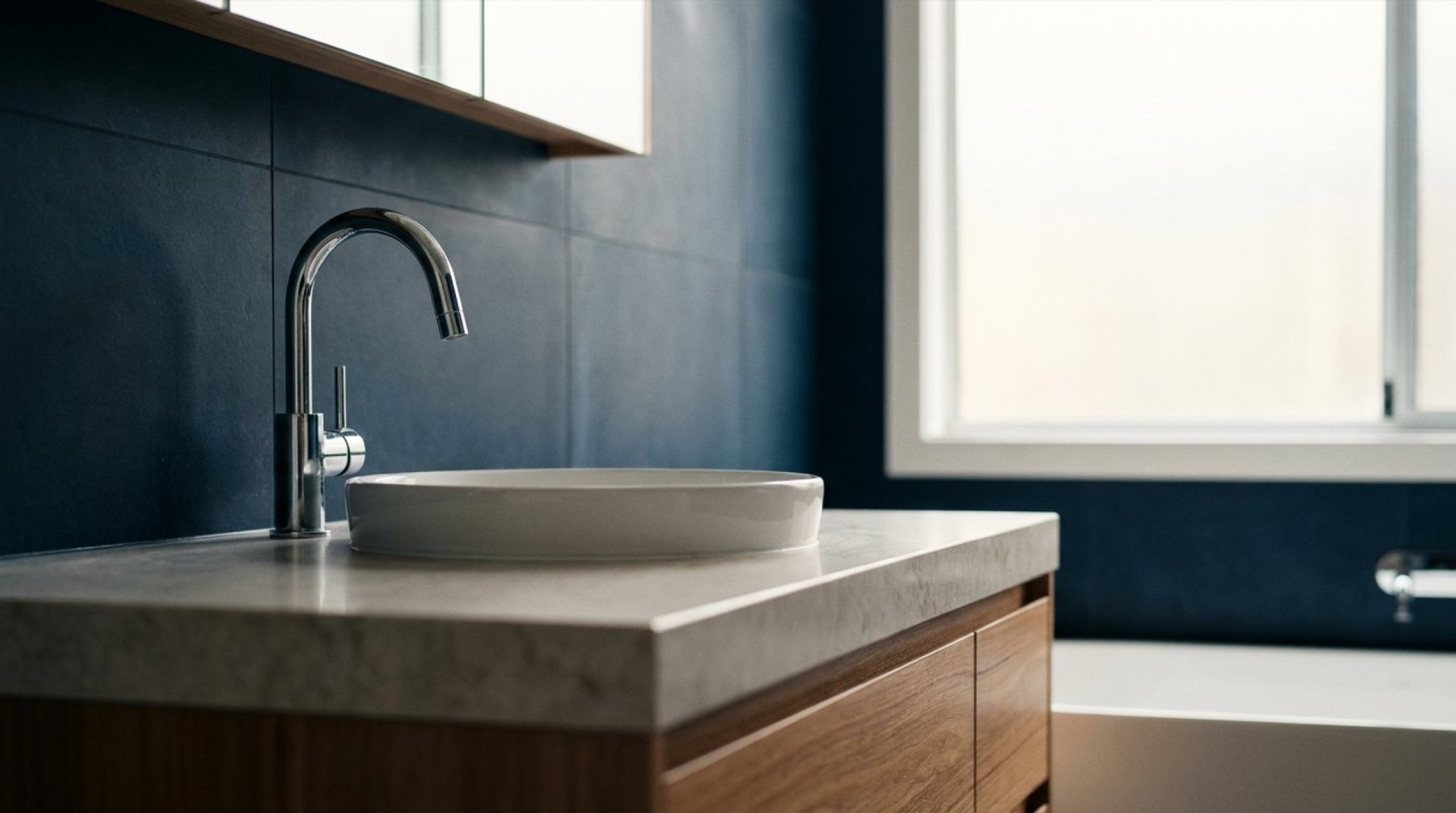 A stone-topped vanity with a round basin and chrome tap against a deep blue wall