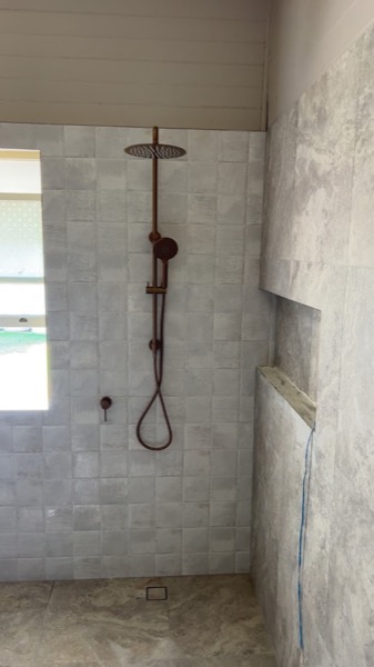 A tiled shower with a rail shower and mixer installed in a new bathroom