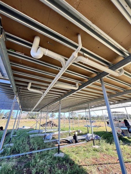 PVC drainage and copper pipework fixed under a steel-framed shed