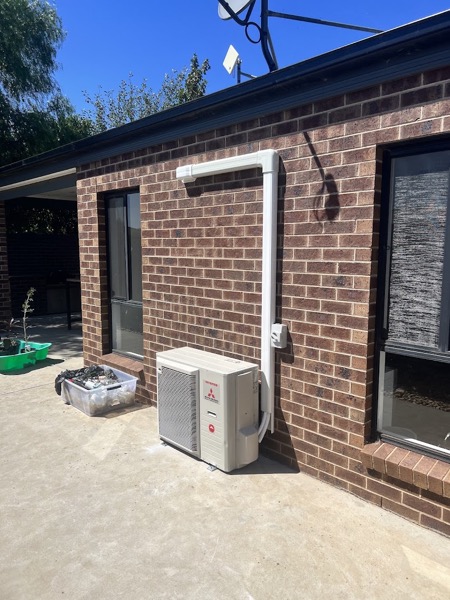 A split system air conditioning outdoor unit installed against a brick wall with new conduit