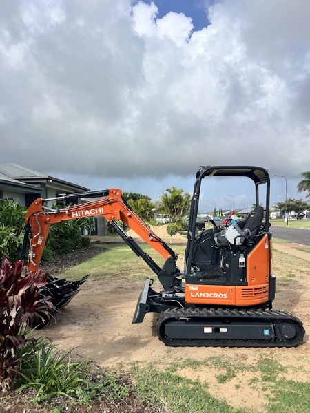 A mini excavator parked beside a garden on a Bundaberg street lined with palms