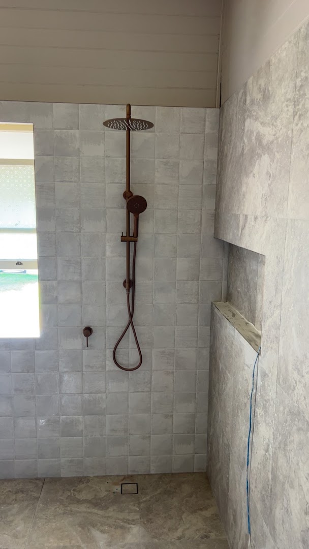 A tiled shower with a rail shower and mixer installed in a new bathroom
