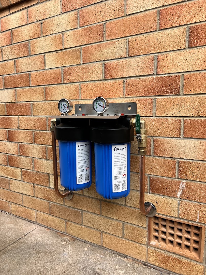 A twin cartridge whole-house water filter mounted on a brick wall with pressure gauges