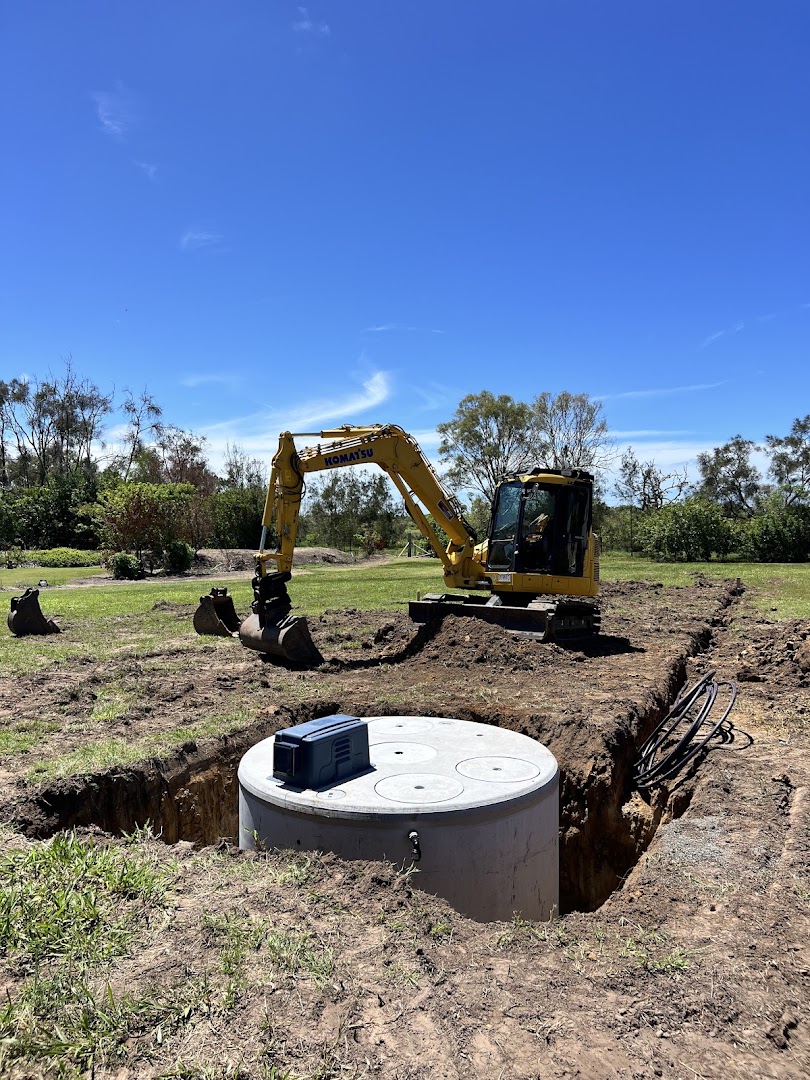 An excavator beside a newly set concrete wastewater treatment tank on a rural block